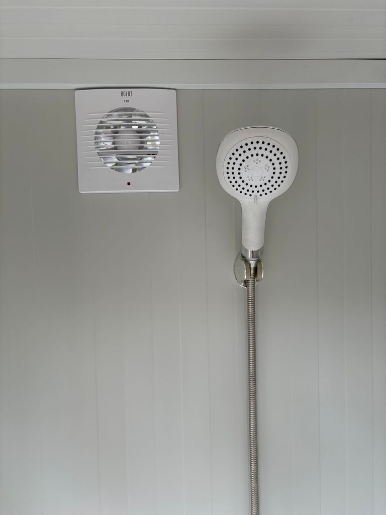 Binnenzijde van een duo mobiele douchecabine unit met douchekop en ventilatie zichtbaar