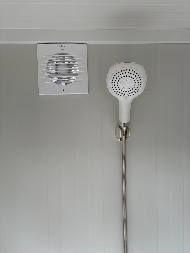 Binnenzijde van een duo mobiele douchecabine unit met douchekop en ventilatie zichtbaar
