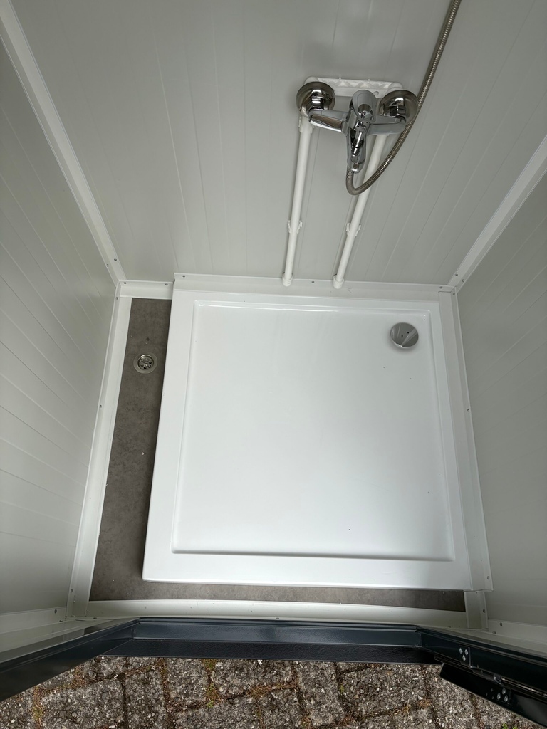 Onderzijde van de binnenkant van een mobiele douchecabine unit met vloerput, mengkraan en onderkant van de douche zichtbaar