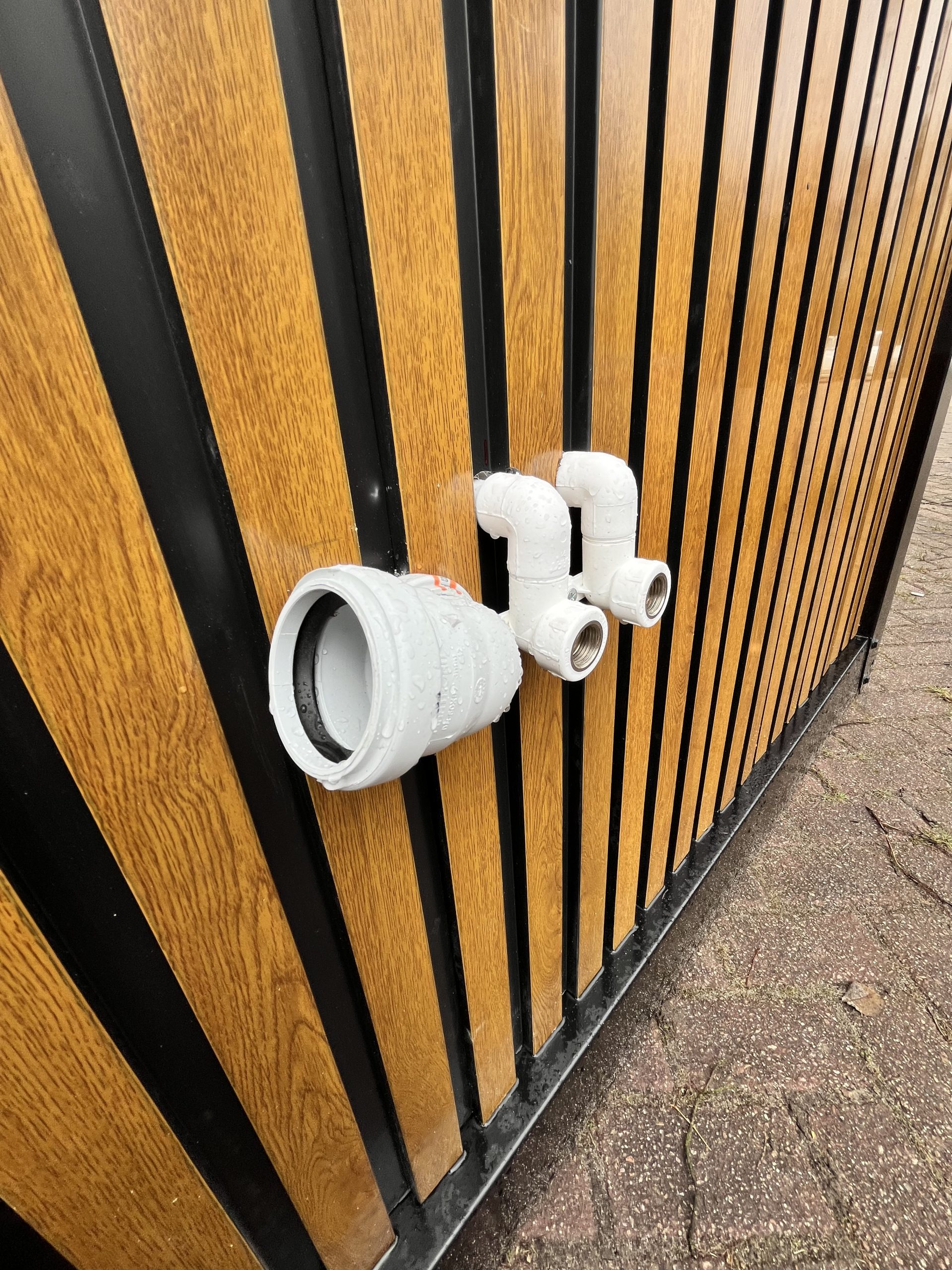 Close-up van zijkant van maatwerk sanitairgebouw met water- en elektra-aansluitingen en koppelingen