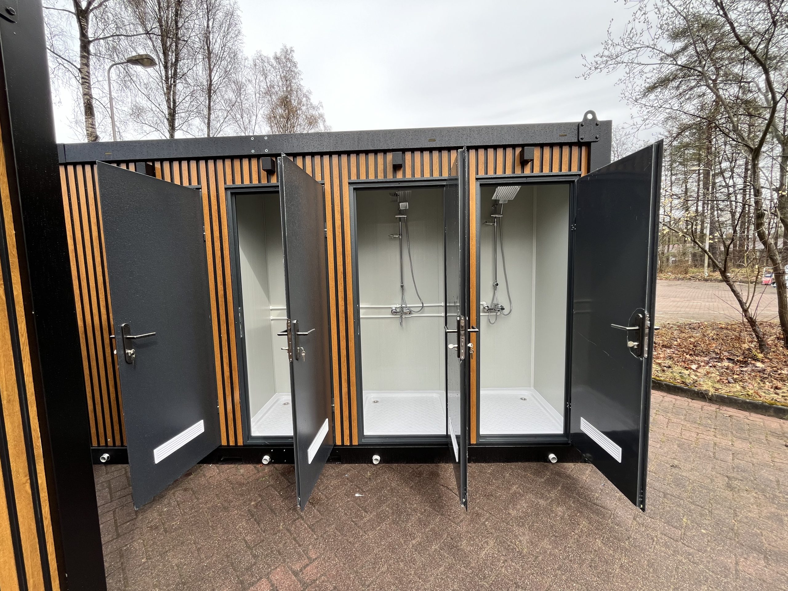 Doucheruimtes in maatwerk sanitairgebouw met geopende deuren en zicht op de binnenruimte