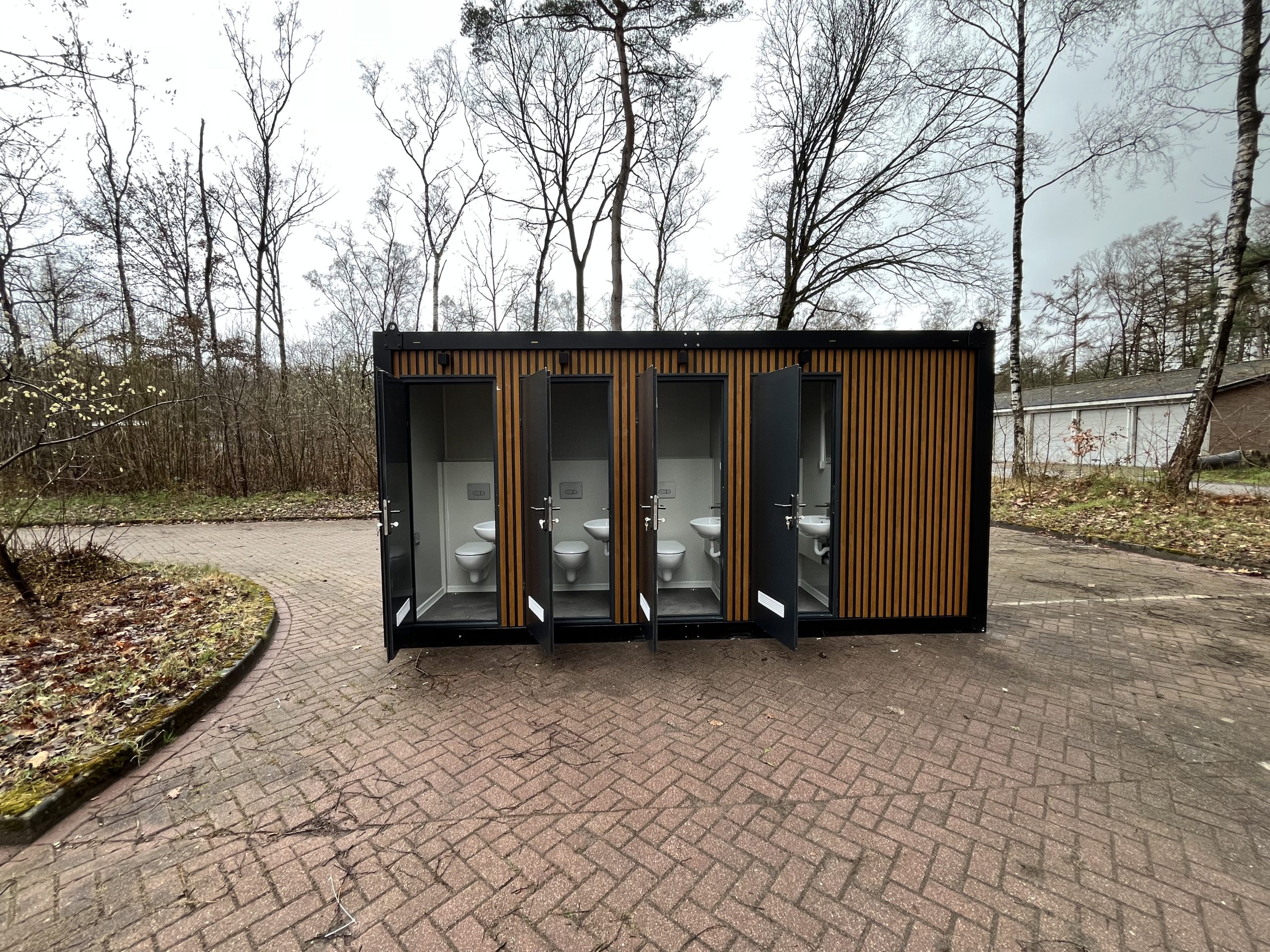 Toiletruimtes in maatwerk sanitairgebouw met geopende deuren en zicht op de binnenruimte