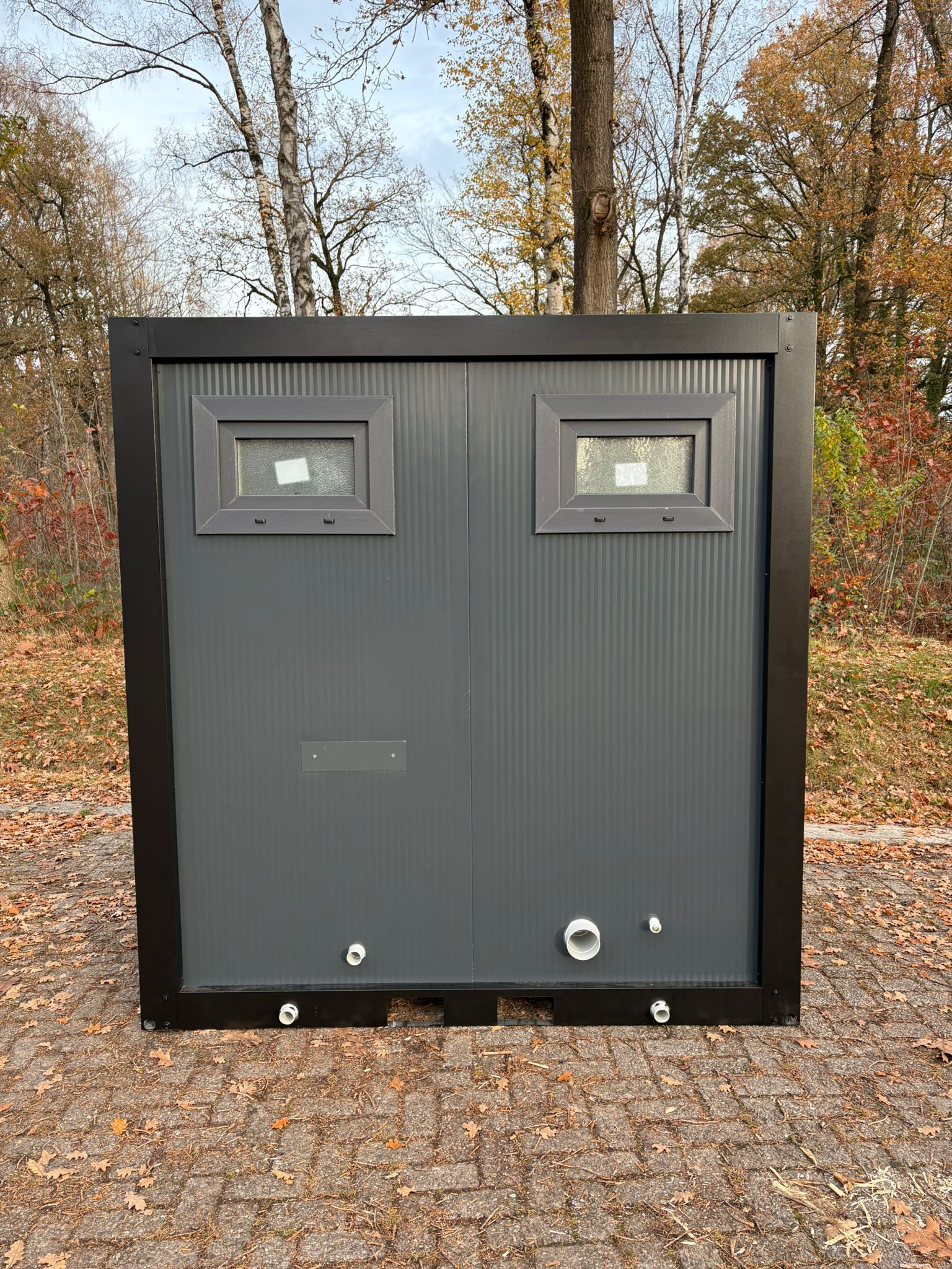 Aansluitingen aan de achterzijde van de buitenzijde van een toilet- en urinoirunit.