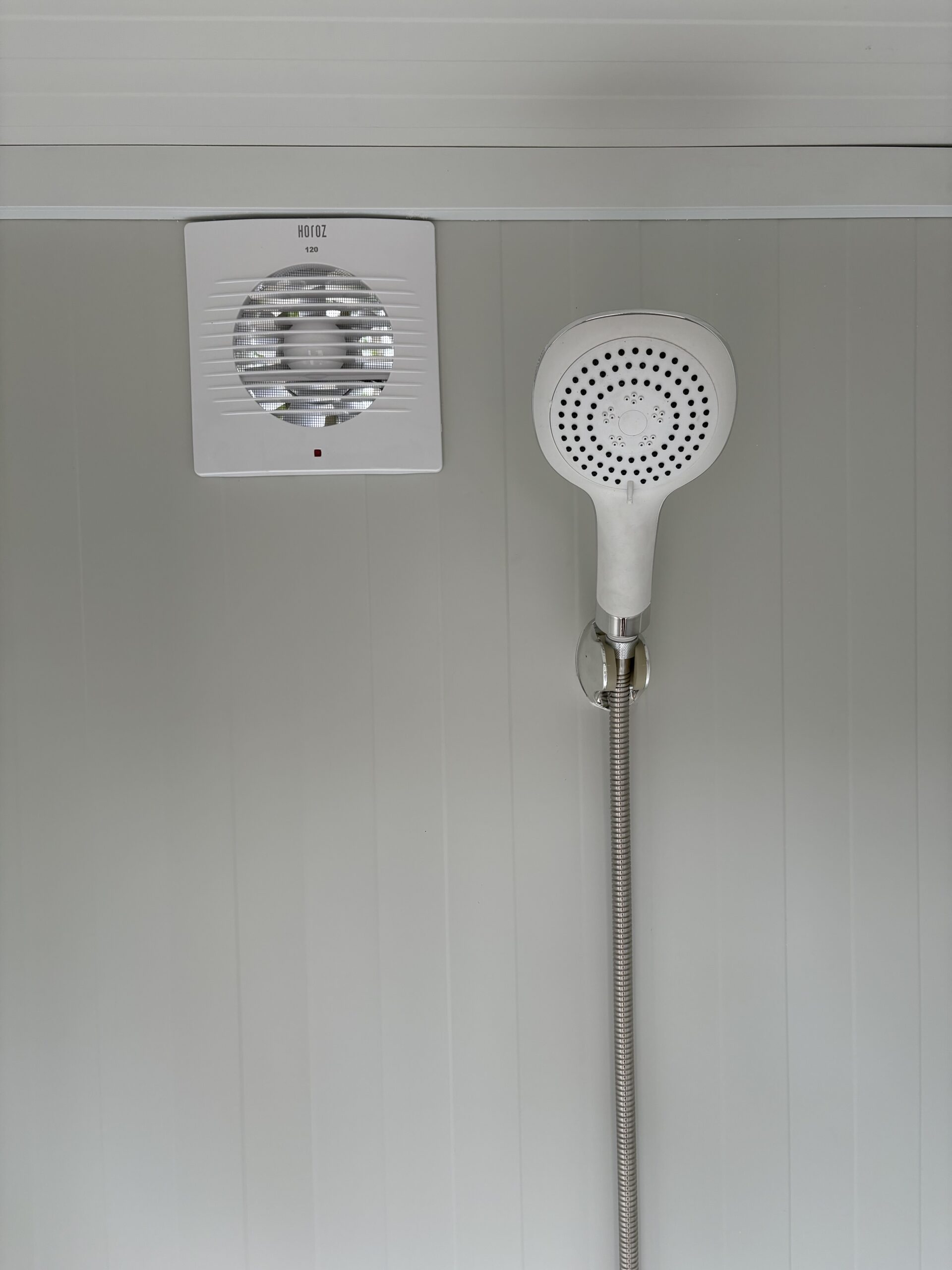 Binnenzijde van een mobiele douchecabine unit met douchekop en ventilatie zichtbaar