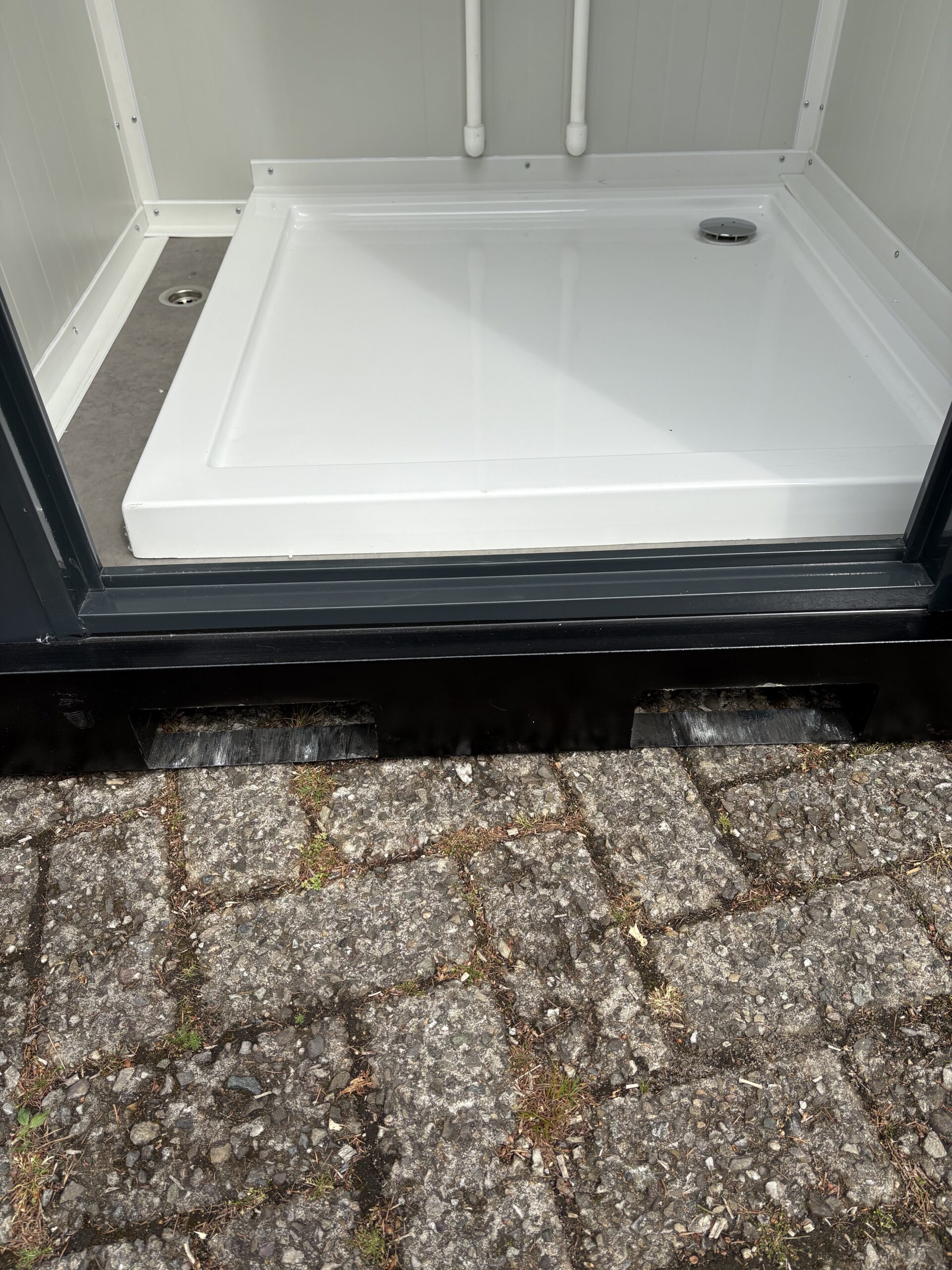 Detail van de drempel, onderzijde van de douche en vloerput in de douchecabine van een mobiele wc- en douche unit