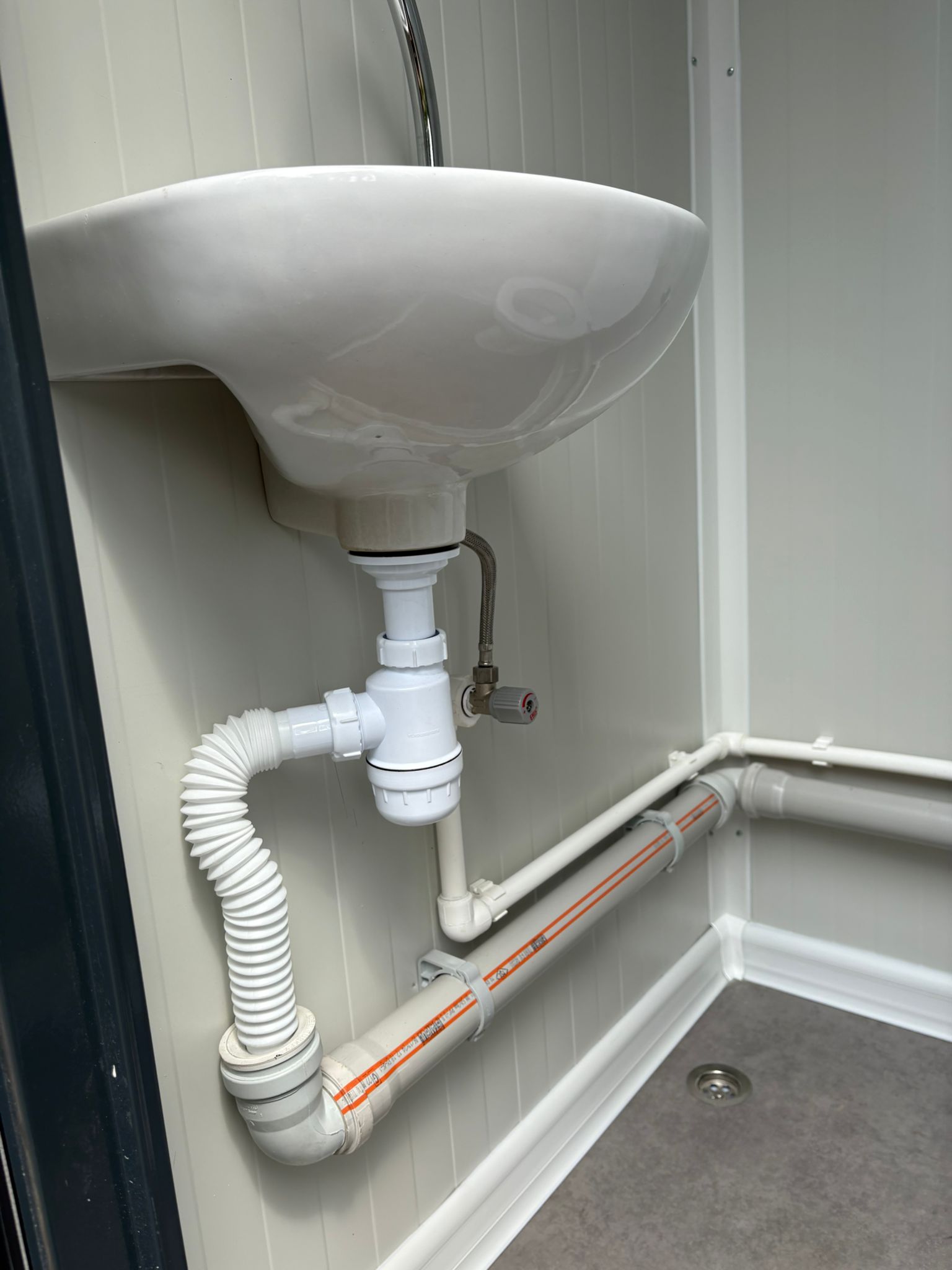 Binnenzijde van de toiletcabine in een mobiele wc- en douche unit met wastafel en zichtbaar leidingwerk